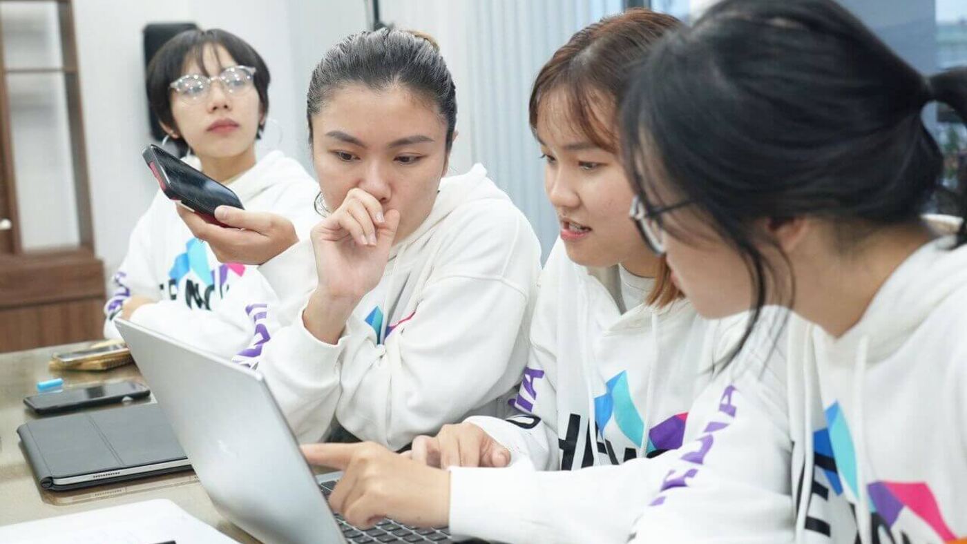 Các bạn nữ MONA mặc hoodie cùng chuẩn bị nội dung trên laptop